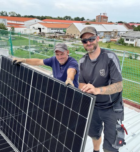 Glückliche Solarteure halten ein Solar-Modul auf einem Dach in Bad Harzburg